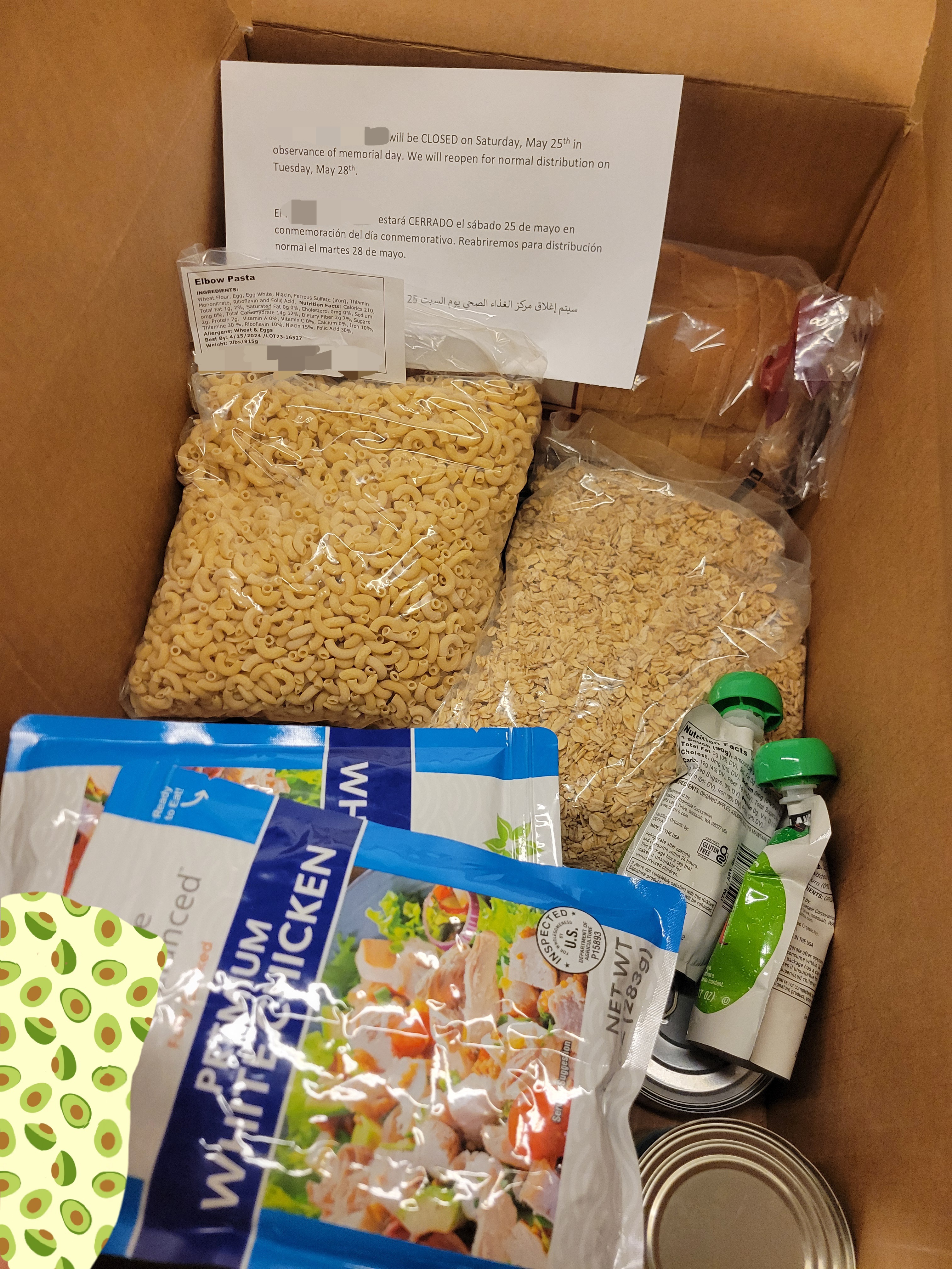 Bread, pasta, canned goods, oats, pouches of chicken with a paper holiday closure notice in a cardboard box.